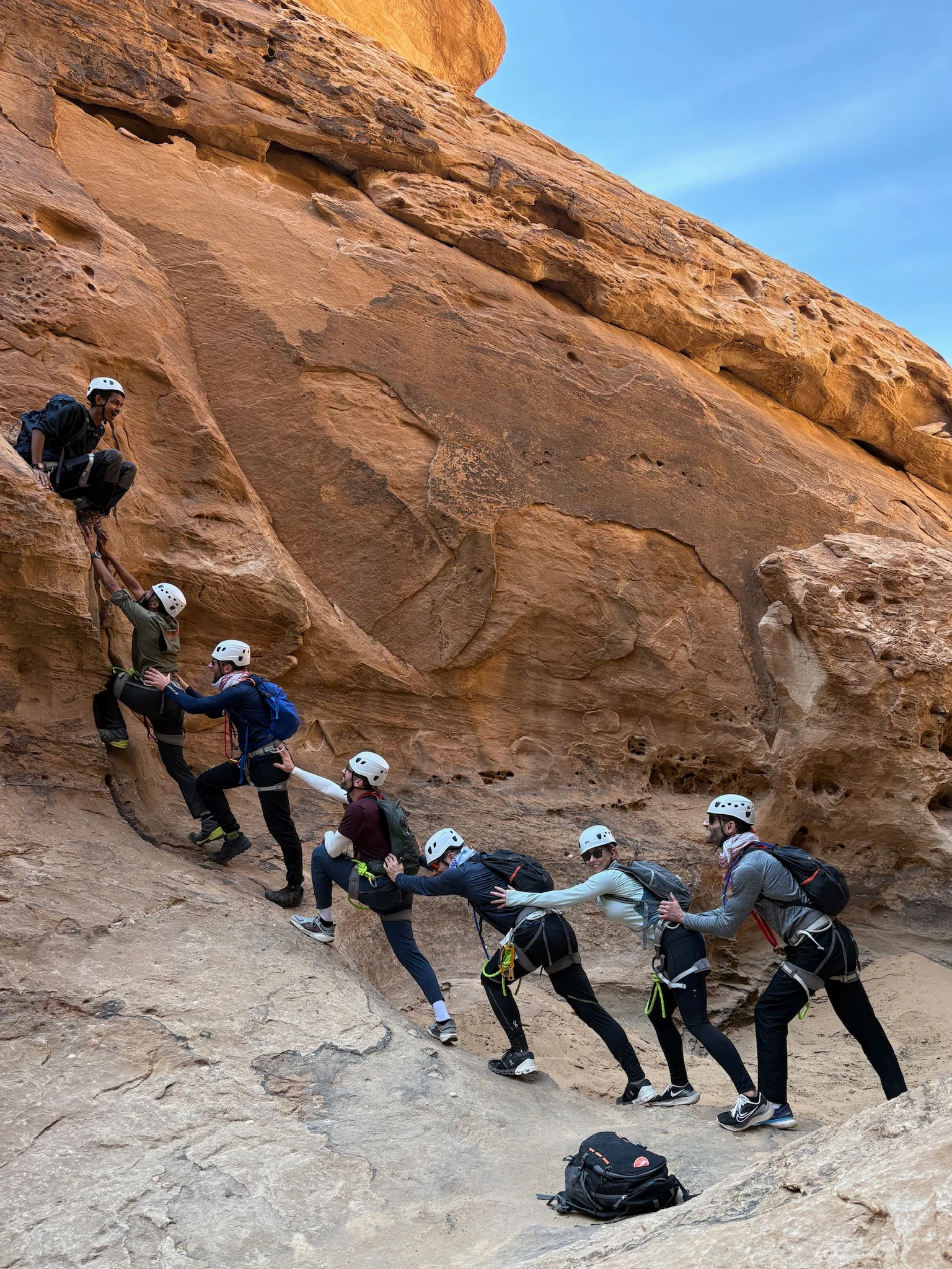 An executive team forming a human chain to help each other up a rock face