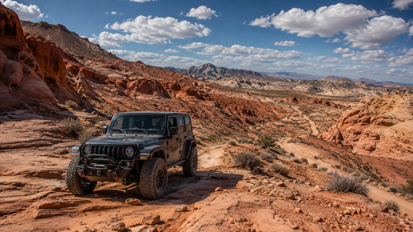 A Jeep Wrangler Rubicon on red-rock desert terrain in the Mojave outside Las Vegas, mountains and open sky beyond.